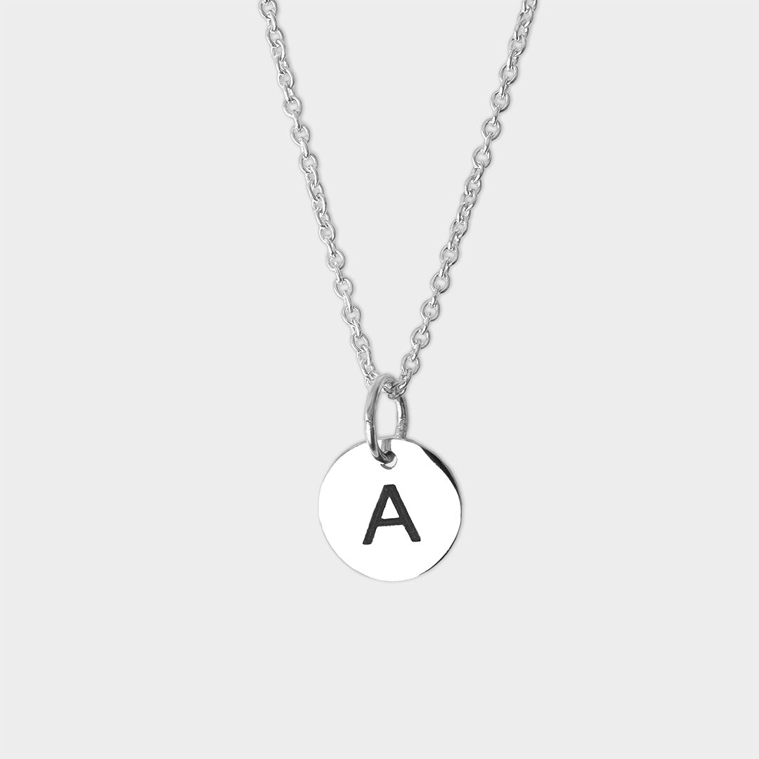 A silver initial necklace with a round silver disc pendant engraved with the black capital letter 'A'