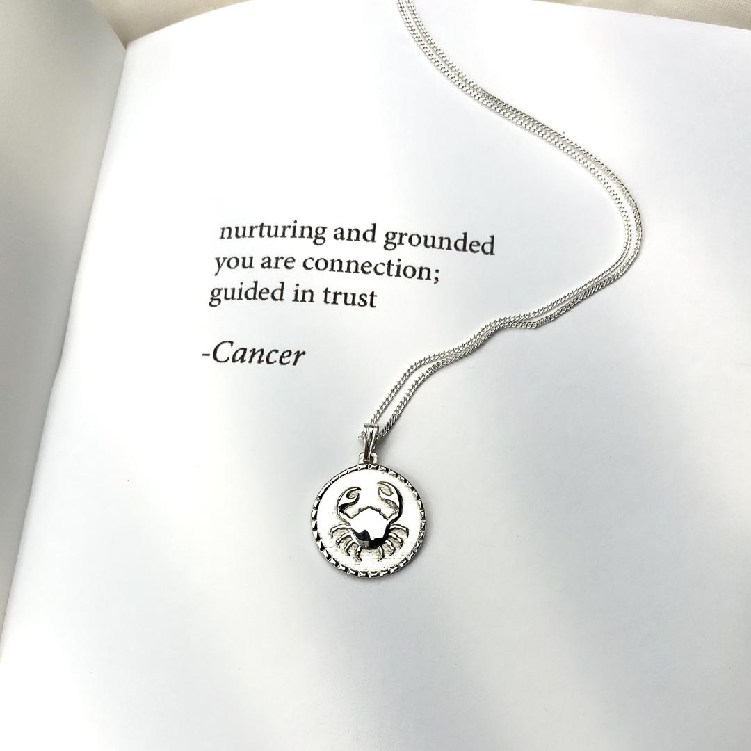 cancer star sign necklace pendant sterling silver jewellery on book with poetry