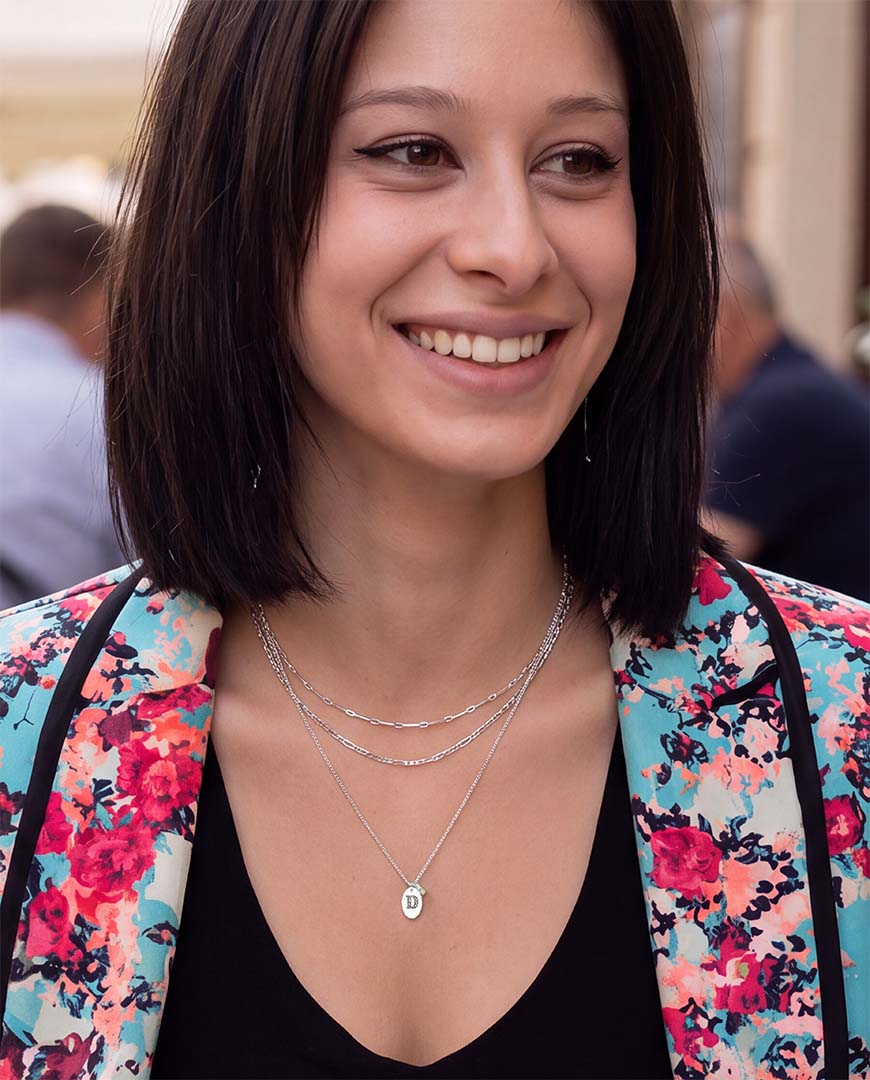 A smiling woman wearing layered silver necklaces, including the Loveletter initial necklace in silver.