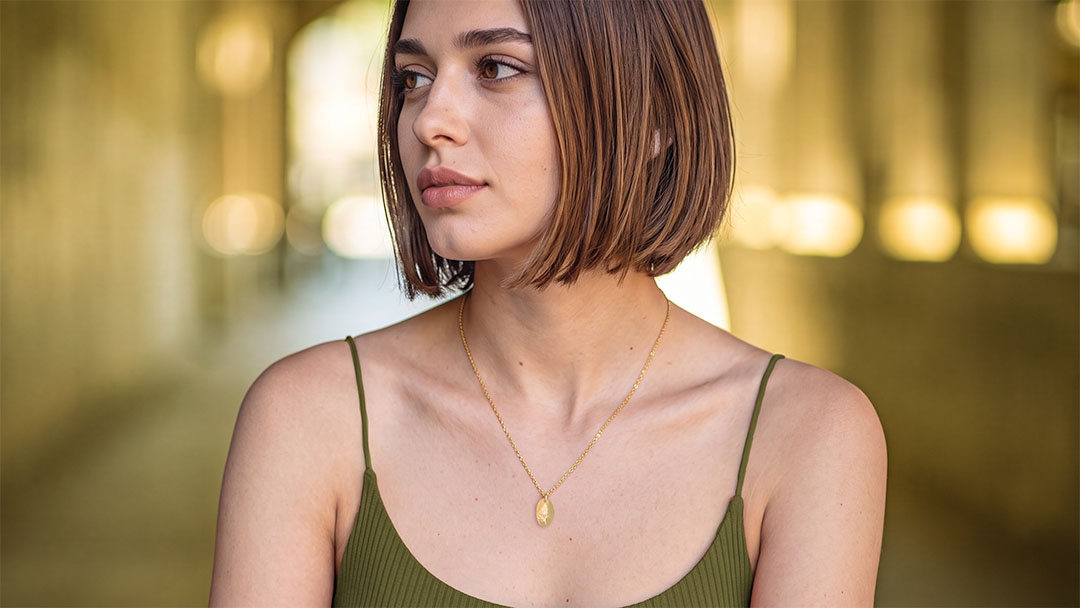 A woman with a short brown bob haircut wearing a gold oval pendant necklace, the Australian native flower necklace by birthmonth in gold by sixD