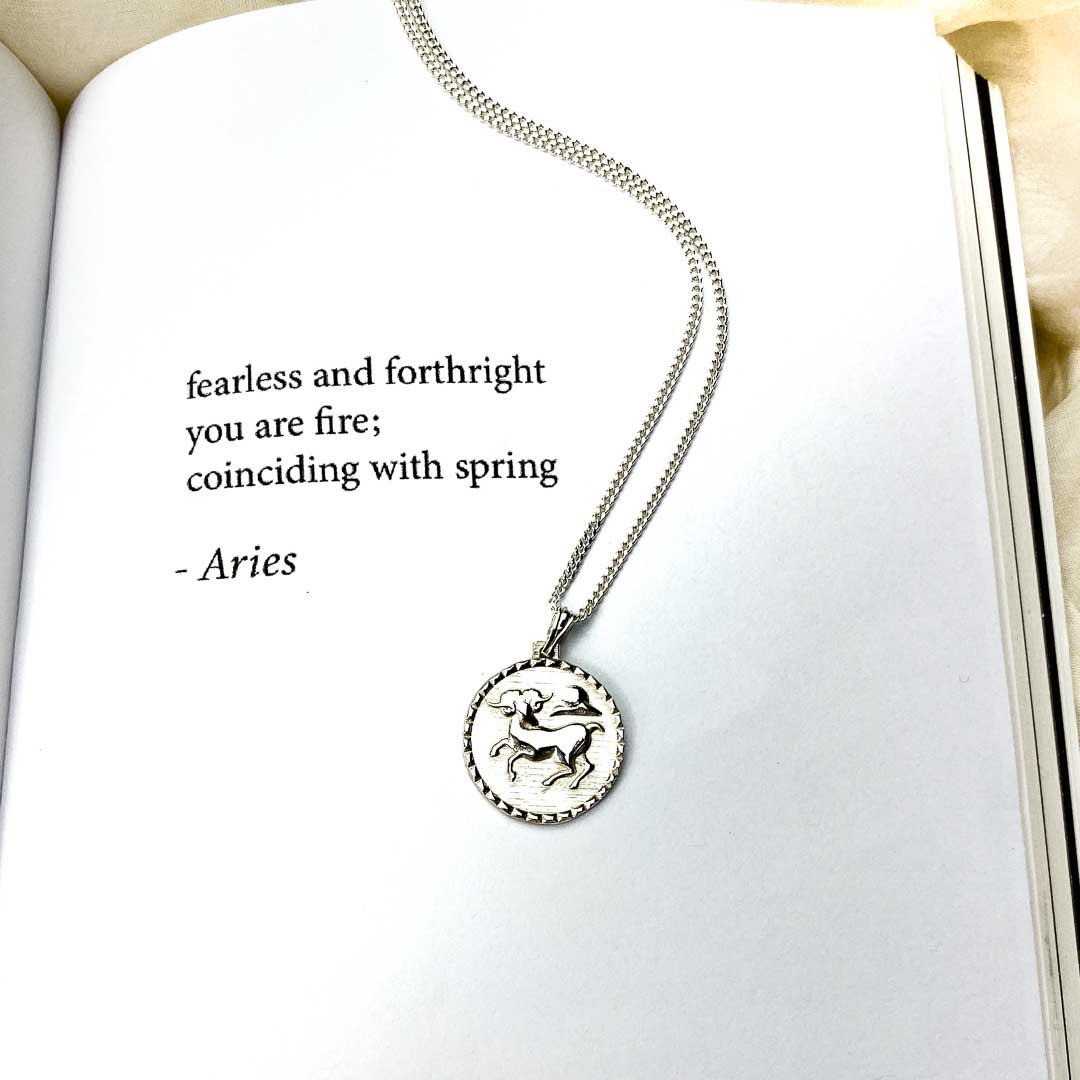 The Aries star sign necklace pendant sterling silver jewellery on book with poetry