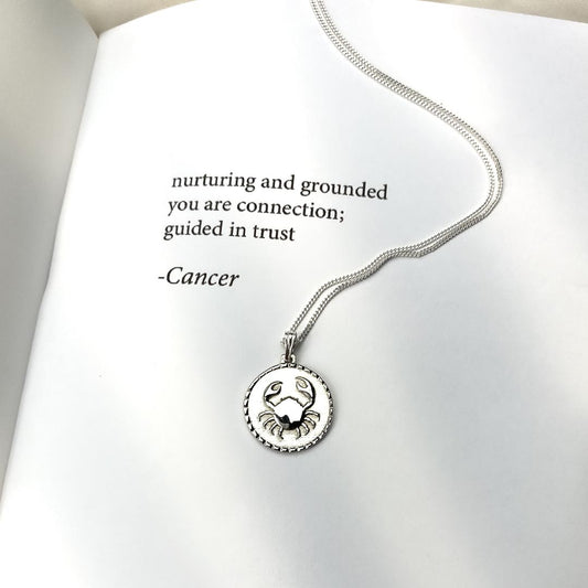 cancer star sign necklace pendant sterling silver jewellery on book with poetry