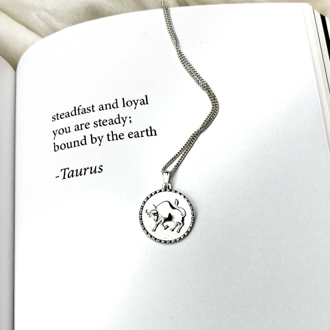 Taurus star sign necklace pendant sterling silver jewellery on book with poetry